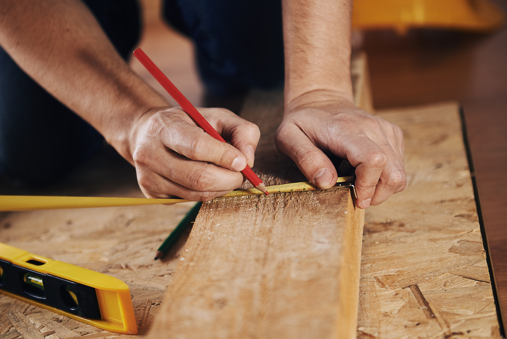 Craftsman measuring wooden plank with ruler on the floor.