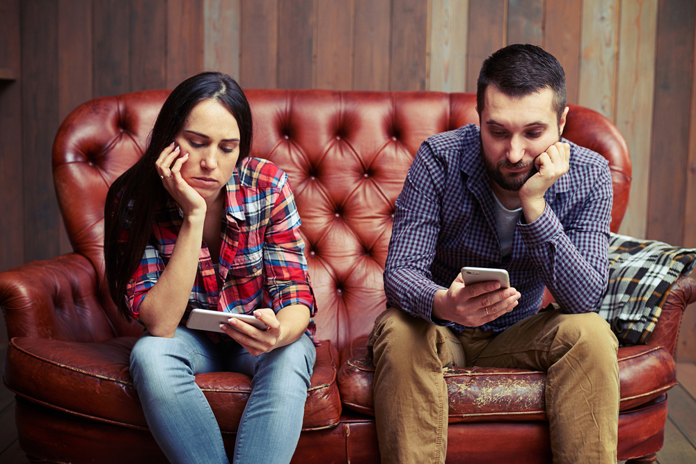 bored young couple sitting on couch and looking at their phones